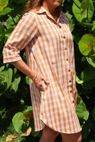 Kaunaʻoa Rust dress with a Palaka print, three-quarter sleeves, and button-down front. Hand in pocket, wearing a bracelet.