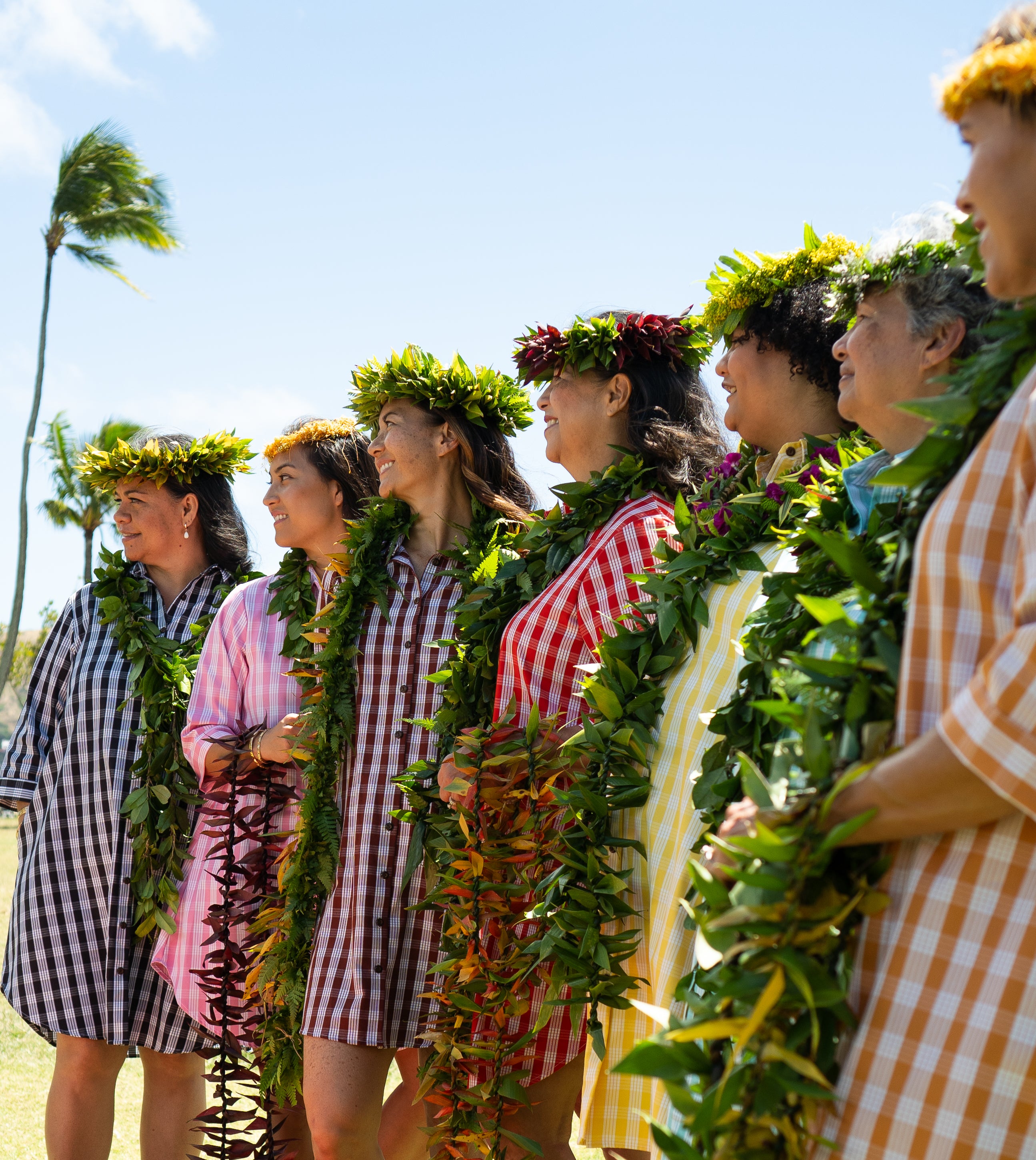 7 Models wearing the The Moana Collection Dress in a variety of colors outside while adorned with Ti Leaf Lei