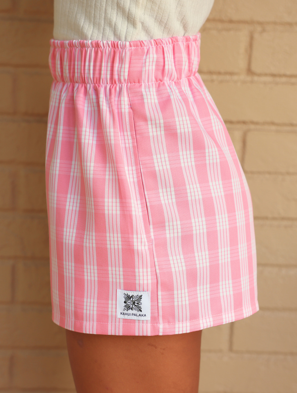 Wahine Holoholo Shorts 2.0 in Lokelani Light, featuring a pink Palaka print. Side view, elastic waistband, and logo tag visible.