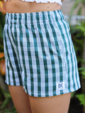 Holoholo shorts with green Palaka print, elastic waistband. Worn outdoors, side view, natural light highlighting the texture.