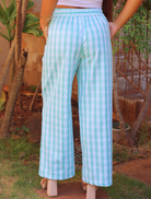 Liʻi Pants with traditional Palaka print, shown from the back. Elastic waistband, wide leg fit. Model outdoors, wearing beige heels and bangles.