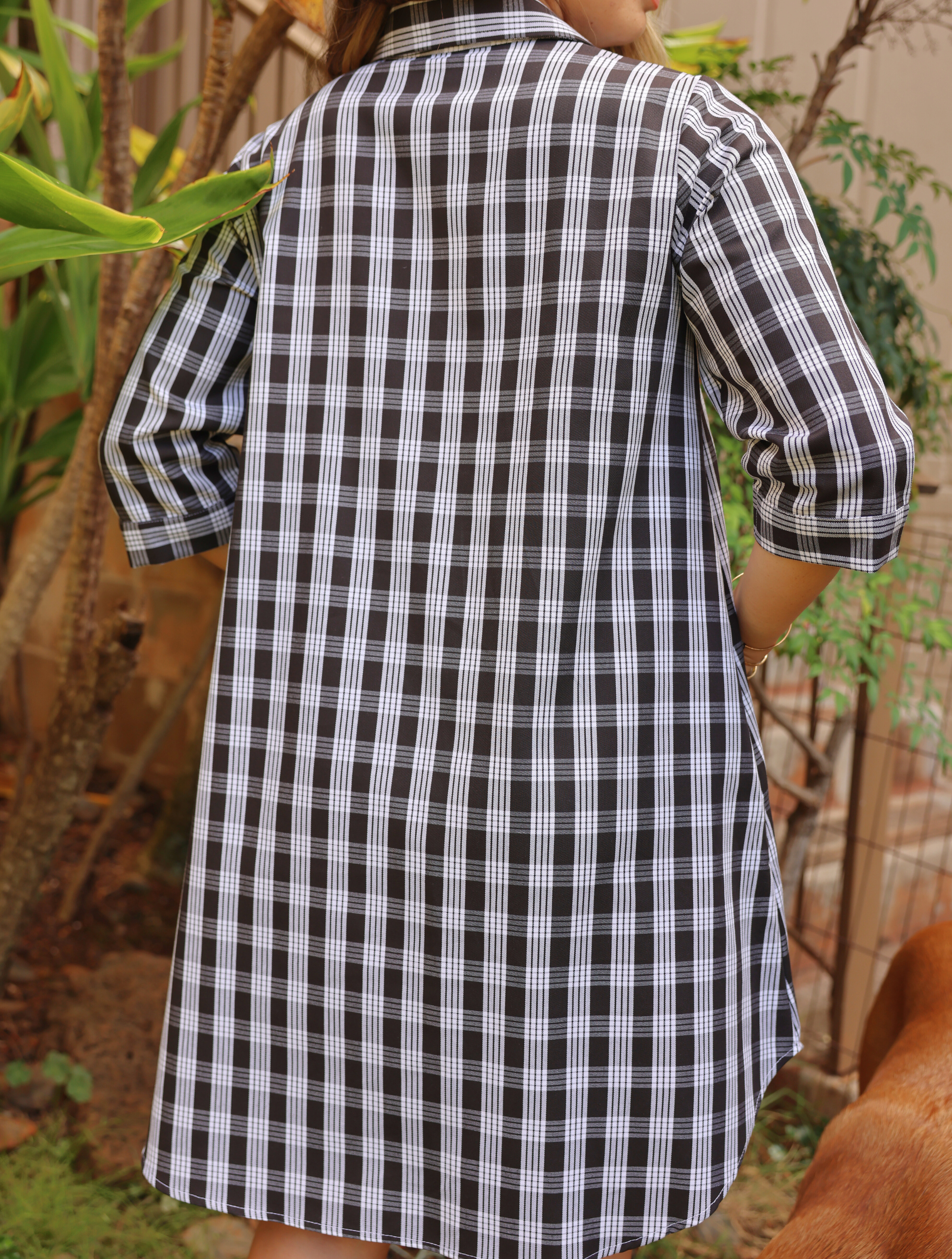 Moana Collection Dress with traditional Palaka print, viewed from the back, three-quarter sleeves. Outdoor setting with greenery.