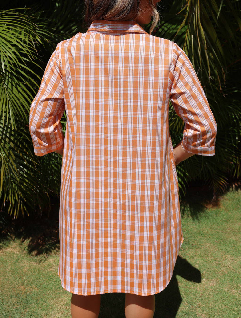Dress with Kaunaʻoa Rust Palaka print, subtle A-line cut. Three-quarter sleeves. Back view, sunlight highlights pattern.