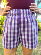Wahine Holoholo Shorts 2.0 with Pōhuehue Palaka print, shown in bright outdoor light. Model holds waistband, showcasing fit.